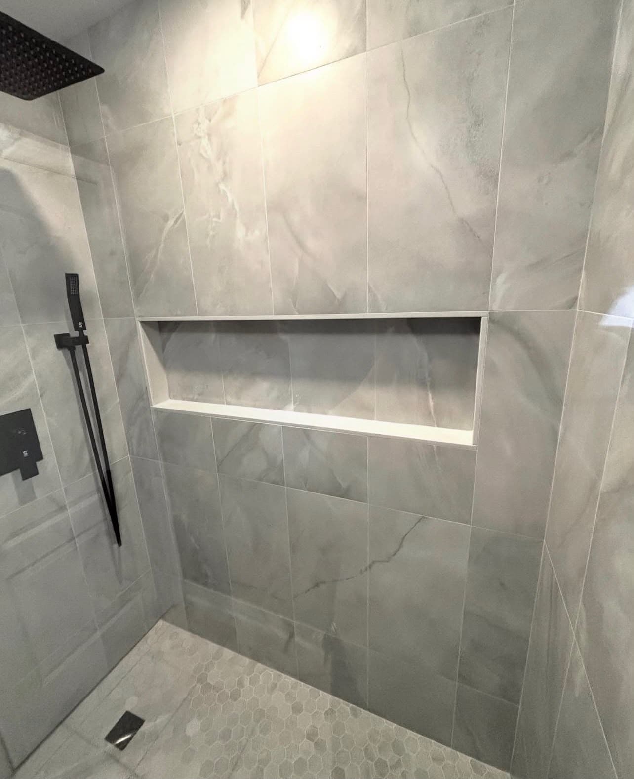 Walk-in shower with large gray marble tile, recessed niche, and matte black rain head installed by Costa Bathroom Remodel in Wimauma, Florida